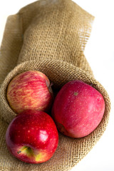 three red apples on the table in sackcloth package on white background 