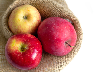 three red apples on the table in sackcloth package on white background 