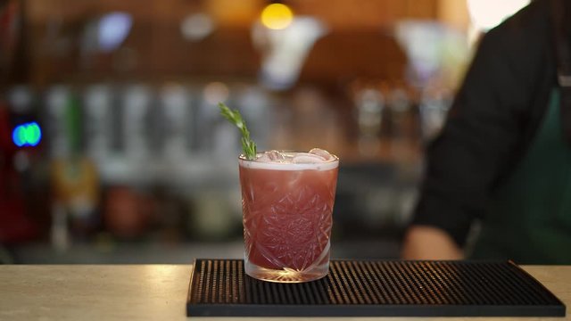 Close up pan shot left to right of bartender decorating a red cocktail in small crystal glass with little branch of pine and red currants. Bartender no face decorating a cocktail