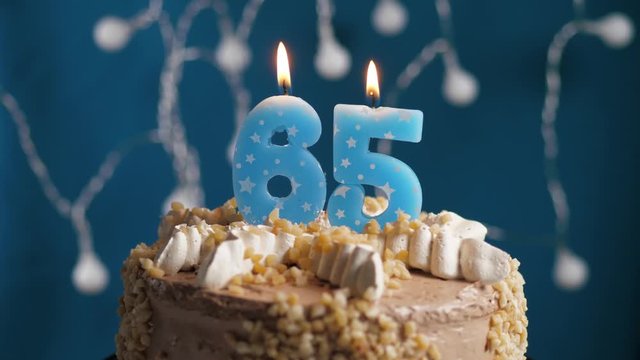 Birthday cake with 65 number candle on blue backgraund. Candles blow out. Slow motion and close-up view