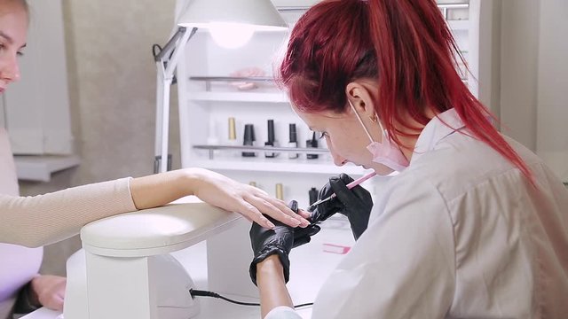 Manicurist woman in cosmetic bath is applying gel on client's nails.