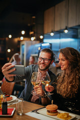 Cute caucasian fashionable couple sitting in restaurant at dinner and taking selfie.