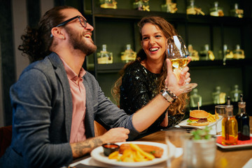 Cute caucasian couple sitting in restaurant and cheering with wine