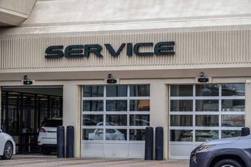 White cars entering an automobile service center garage through an open garage door. Two other doors are closed