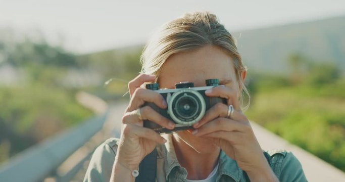 Portrait of an attractive happy smiling woman outdoors taking a picture with her vintage camera, happy outdoors photographer traveling and taking photos