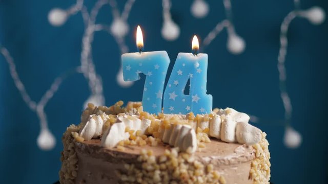 Birthday cake with 74 number candle on blue backgraund. Candles blow out. Slow motion and close-up view