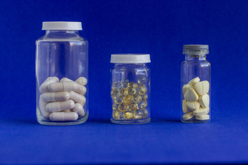 Different  medical pills in glass jar and scattered  on a blue  background. Viral infection season. Traditional  medicine, healthcare and wellness concept.