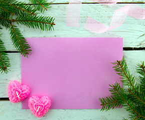 It's time for a holiday! Festive blank pink greeting card on white wooden background with decorative ribbon, pink candles and green Christmas tree. Top view..