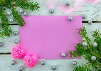 It's time for a holiday! Festive blank pink greeting card on white wooden background with decorative ribbon, pink candles and green Christmas tree. Top view.