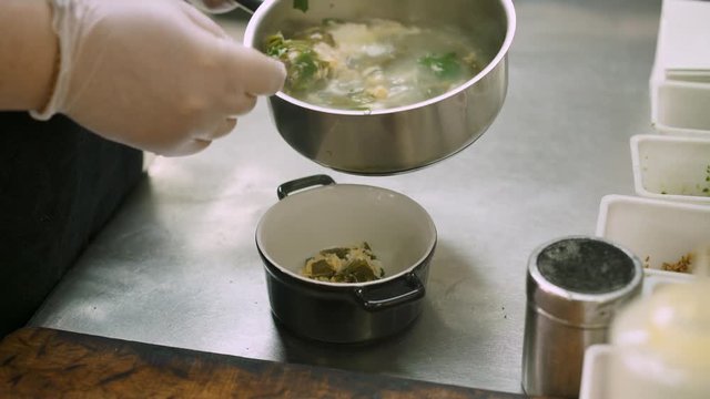 Close up handheld shot of chef hands in white rubber gloves pouring ukha soup into a plate. Ukha fish soup cooked in the restaurant ready to serve