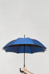 A man holds a blue umbrella in his hand against a gray wall. Open space above the umbrella. Concept...