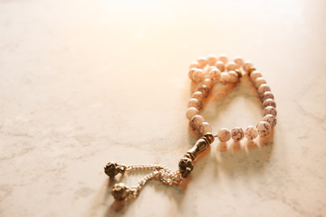 Conceptual close up shot of prayer beads and bright sun flare from the back in the evening with copy space. Selective focus with shallow depth of field. Image may contain soft focus and noise texture.
