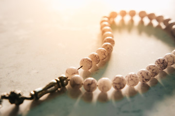 Conceptual close up shot of prayer beads and bright sun flare from the back in the evening with copy space. Selective focus with shallow depth of field. Image may contain soft focus and noise texture.