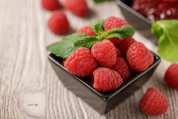 Ripe raspberries in a dark bowl on an old wooden background