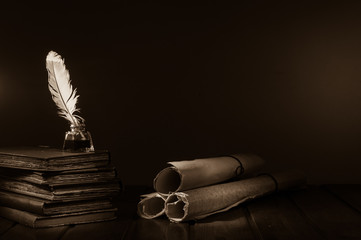 Quill pen and rolled papyrus sheets on a wooden table with old books, sepia effect - 311624703