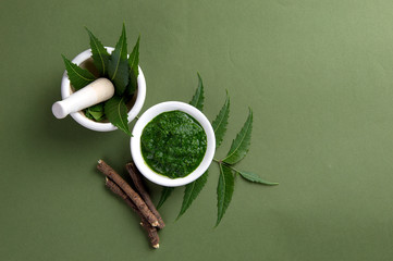 Medicinal Neem leaves in mortar and pestle with paste and twigs on green background