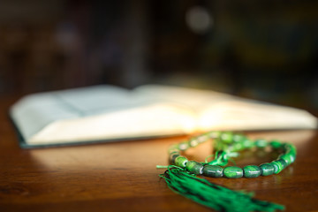 Closeup of rosary beads on the wooden table with blurred quran in the background. Selective focus with small depth of field. Islamic concept.