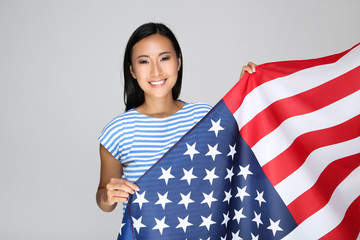 Young woman holding American flag on grey background