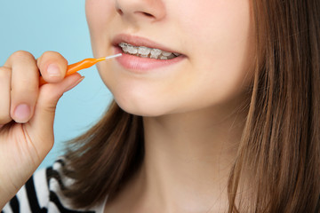 Young girl with dental braces holding toothbrush on blue background