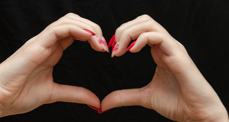 Red manicure on a black background. Fashionable model. Beautiful hands. Heart. Valentine's Day. Love.