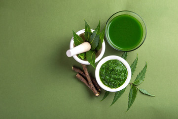 Medicinal Neem leaves in mortar and pestle with neem paste, juice and twigs on green background