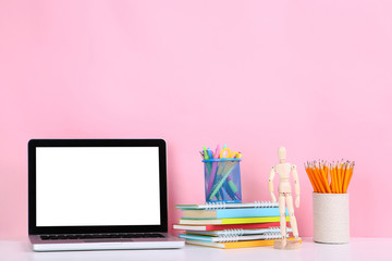 Laptop computer with office supplies and wooden figure on pink background