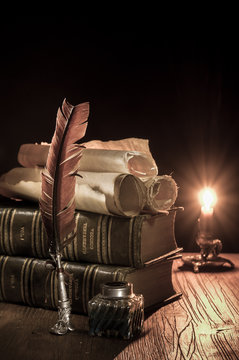 Quill pen and a rolled papyrus sheet with old books at candle light, vintage effect