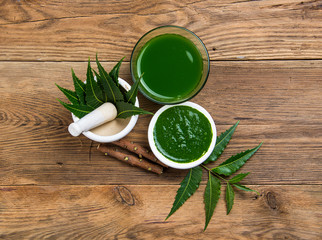 Medicinal Neem leaves in mortar and pestle with neem paste, juice and twigs on wooden background