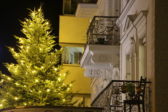 Nachtaufnahme, ein beleuchteter Weihnachtsbaum vor Hausfassaden in der Stadt