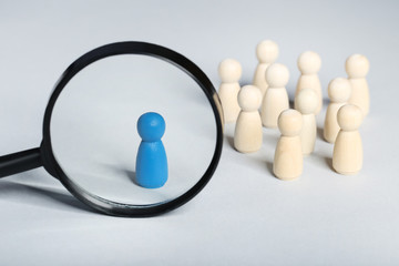 Leader concept. Wooden figures with loupe on grey background