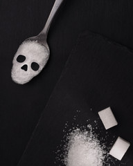 Skull shape sugar spoon on black stone background. Sugar addiction concept