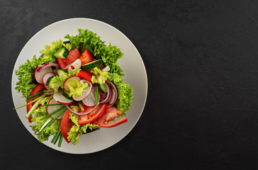 Fresh vegetable salad in a black cup on a gray dish. View from above. Copy space. Black background.