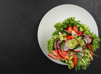 Fresh vegetable salad in a black cup on a gray dish. View from above. Copy space. Black background.