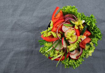 Fresh vegetable salad in a black cup. View from above. Copy space. Blue fabric background.