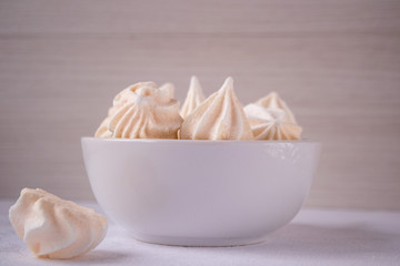 Homemade beige meringues in white ceramic bowl on white table. Meringue cookies. Crispy dessert. 