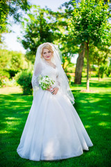 Young bride wearing gorgeous wedding dress, playing with veil. plays a wedding dress. Dress develops in the wind. Happy blonde bride in park