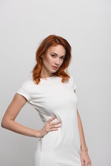 Beautiful redhead girl in a beige dress posing in front of the camera. Portrait on a neutral light background, space for text