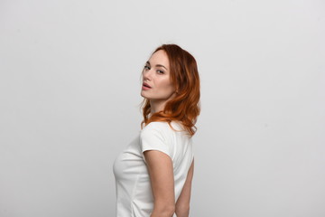 Beautiful redhead girl in a beige dress posing in front of the camera. Portrait on a neutral light background, space for text