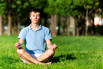 Naklejka na ściany i meble Half naked man sitting on green grass, meditating and doing yoga pose