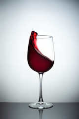 Creative photo of wine glass with storm in a glass on white background. A wine glass filled wine and a wave of wine flies from a wine glass. Wine glass stay on black glass sheet.