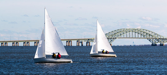 Two two person sailboats sailing toward West Islip with the Great South Bay bridge