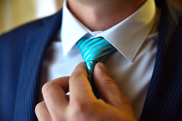 Young man in a blue suit with a white shirt ties a blue tie