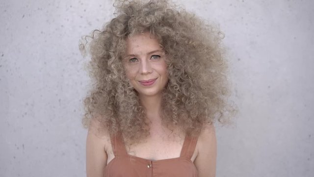 Cute curly blonde with afro hairstyle laughs. plain gray background. emotional photo
