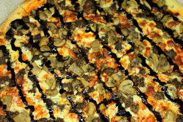 Delicious fresh pizza served on wooden table, brown background with copy space. Top view of a round pizza cut into pieces with mushrooms and meat under stripes of black sauce.