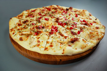 Smoked pizza. chicken, pomegranate berries and cheese. Wooden plate. Gray background. Restaurant