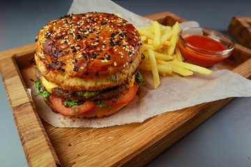 Burger with beef, chicken and french fries. Wooden plate. Gray background. Submission of the restaurant.