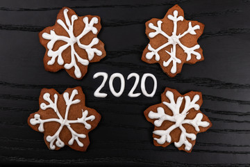 mininalistic concept of Christmas and new year on black wooden background with figures 2020 made with white icing and homemade gingerbread cookies as snowflakes, top view