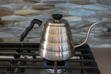 making pour over coffee with a stainless steel kettle on a gas stove