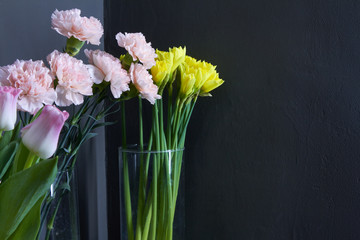 Glass vases with tulips, carnations and daffodils on a dark background, concept of congratulations mother's day, eighth of march