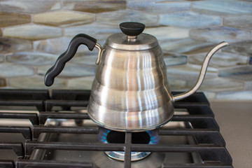 making pour over coffee with a stainless steel kettle on a gas stove